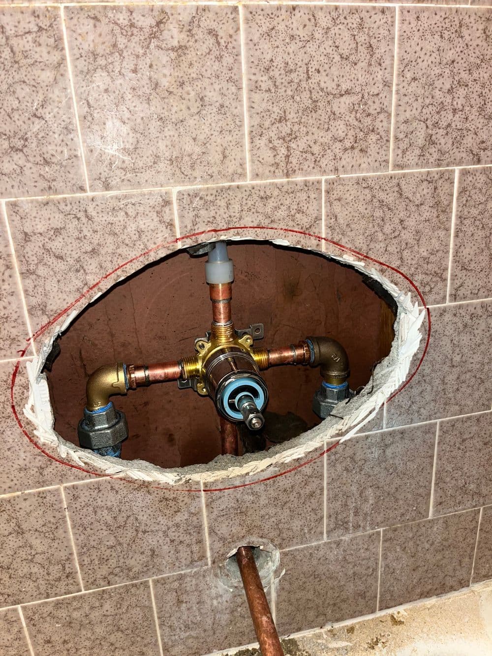 Exposed plumbing valve in wall with copper pipes and fixtures for bathroom installation.