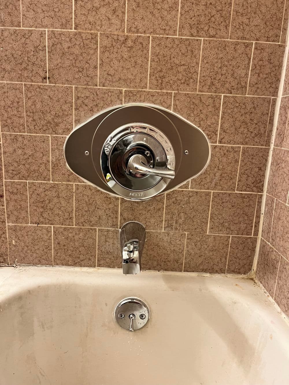 Shower valve and faucet handle installed in a vintage tiled bathtub.