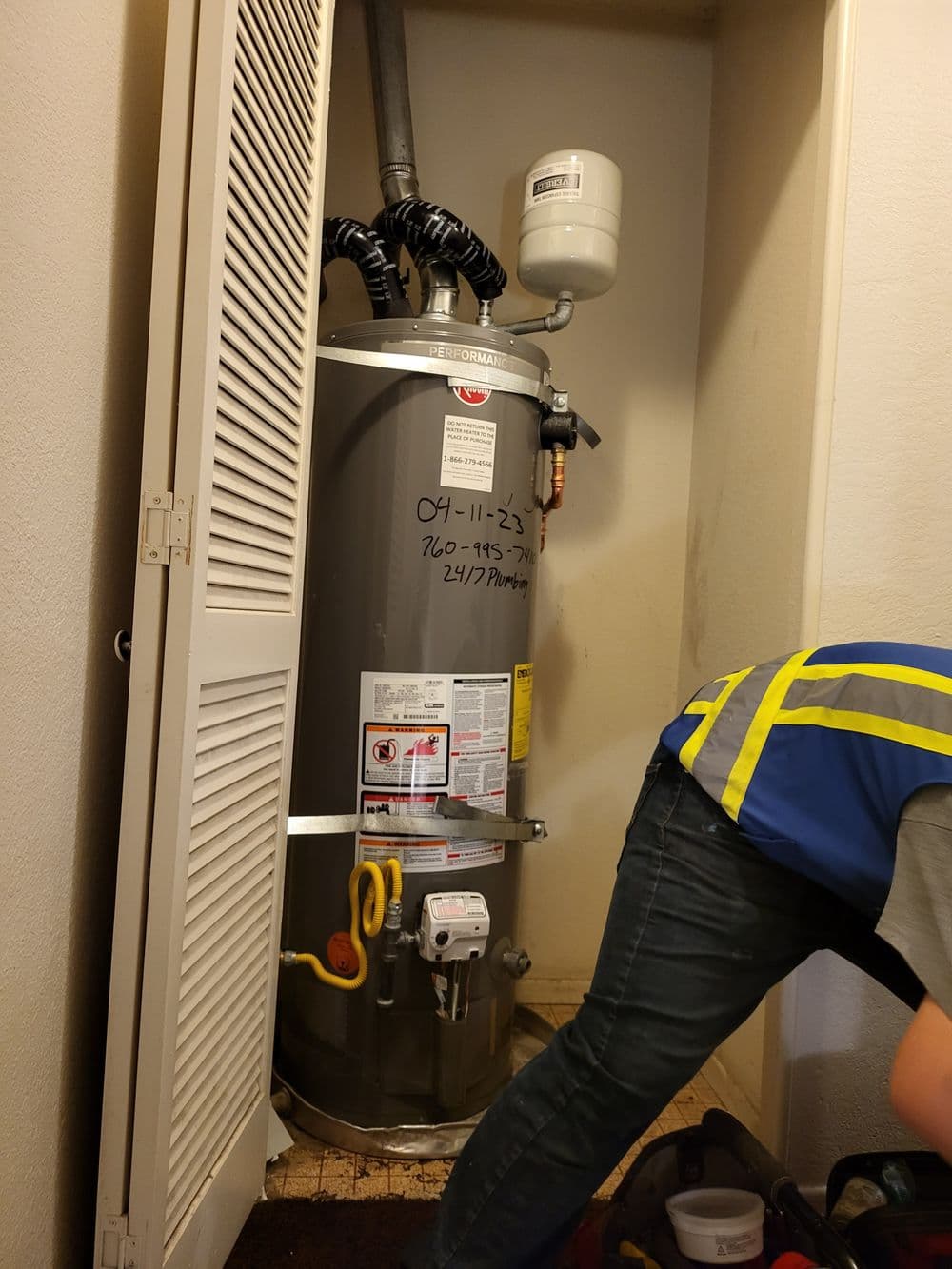 Water heater installation in a small closet with tools and a technician in a safety vest.